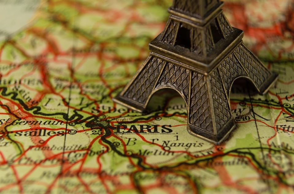 Der Bildausschnitt fokussiert den Sockel eines kleinen Eiffelturm-Souvenirs welches auf einer Frankreichkarte steht und direkt neben Paris positioniert wurde.