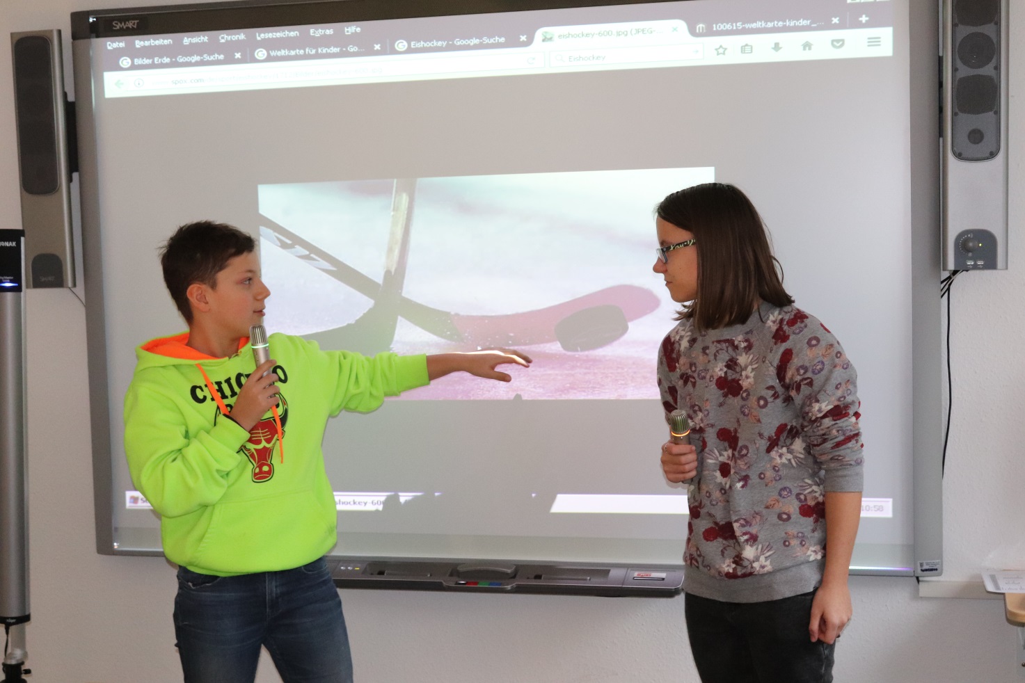 Eine Schülerin und ein Schüler mit Mikrofonen einer Höranlage beim Präsentieren