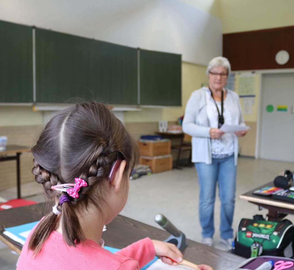 Optimaler Sitzplatz: Schülerin von hinten mit Hörgerät und Lehrerin