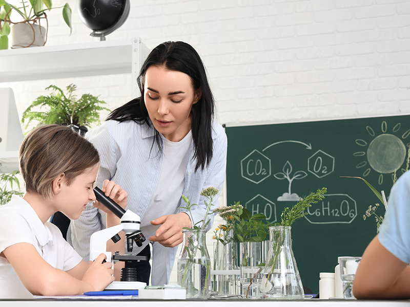 Eine Lehrerin hilft einer jungen Schülerin bei der Arbeit mit dem Mikroskop