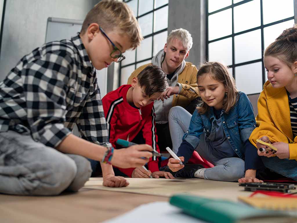 mehrere junge Schüler befüllen dem Boden hockend gemeinsam ein Plakat