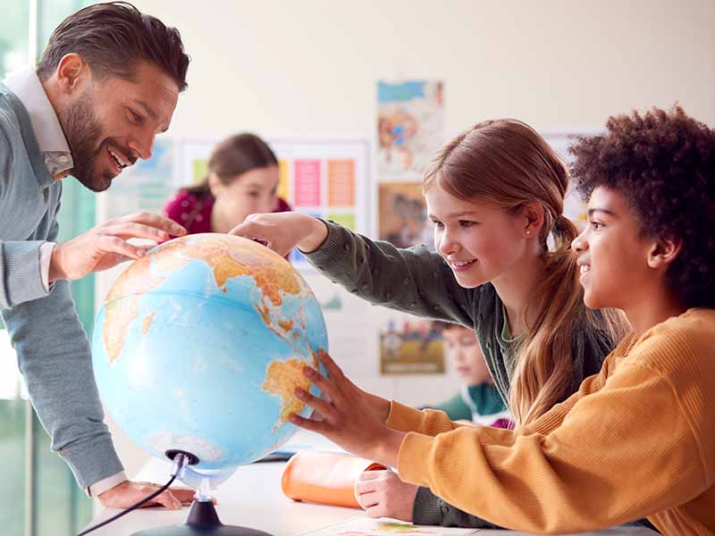 Szene im Klassenzimmer- Ein Lehrer arbeitet zusammen mit Schülern an einem Globus.