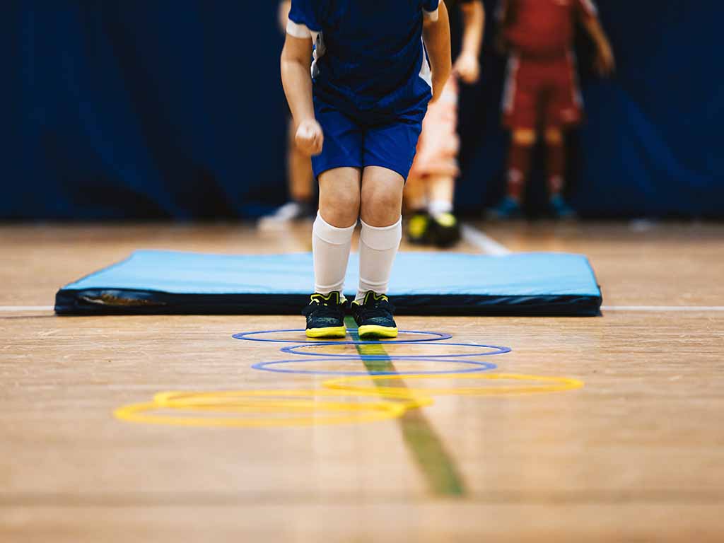 Ein Schüler in der Sporthalle vor einer Bodenmatte. Es sieht so aus als wolle er gleich springen.