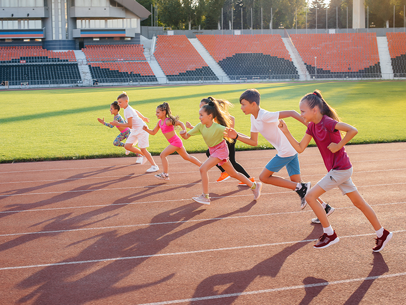 Das Bild zeigt eine Gruppe von Kindern oder Jugendlichen, die auf einer Laufbahn im Stadion starten. Es handelt sich um eine sportliche Aktivität, die den Bereich Leichtathletik, insbesondere einen Sprintwettbewerb, darstellen könnte.