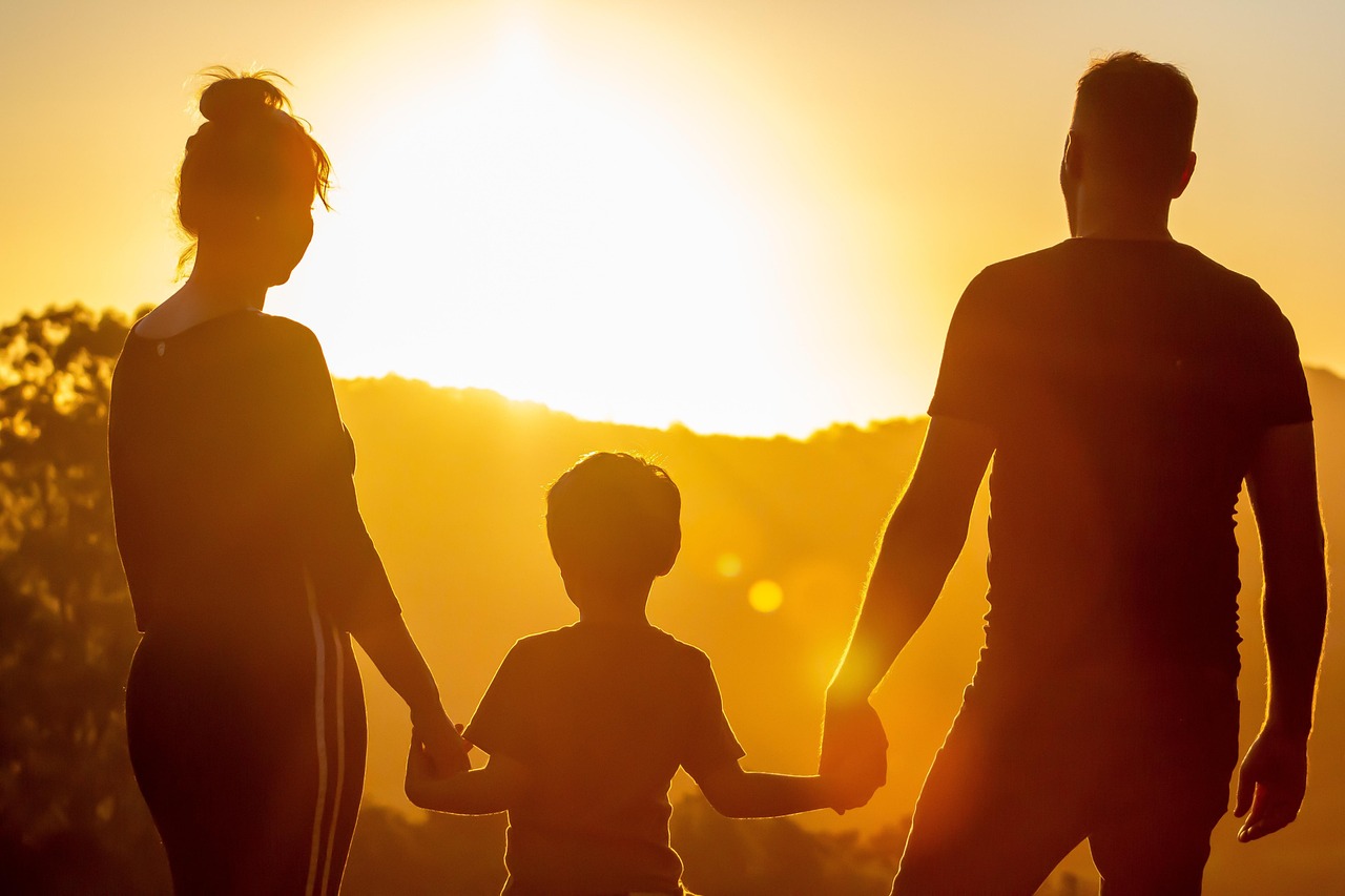 Silhouette einer Familie, die sich bei Sonnenuntergang an den Händen hält, mit einem Kind in der Mitte.