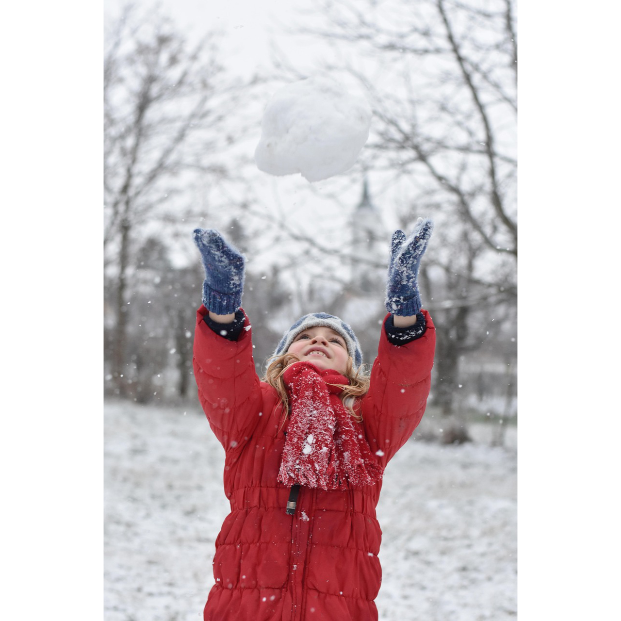 Kind im Winter mit Mütze, Schal und Handschuhen wirft eine Schneekugel in die Luft