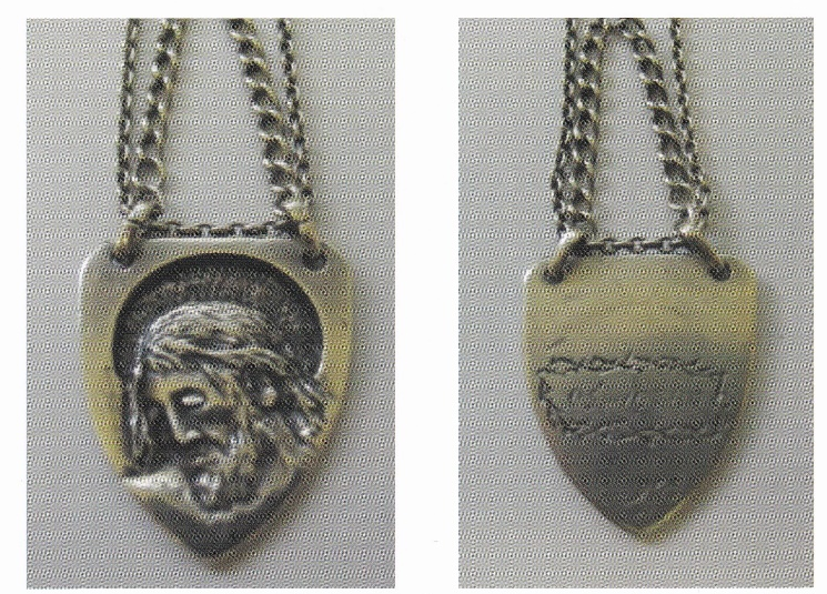 Ein Medaillon mit einer Kette. Die Vorderseite des Medaillons zeigt eine Gravur des Kopfes von Jesus Christus mit einem Heiligenschein. Die Rückseite des Medaillons ist graviert, die Schrift ist nicht gut lesbar.