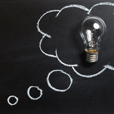 Klare Glühlampe, die in einer Gedankenblase, die mit Kreide gezeichnet wurde, auf einer Tafel plaziert ist.