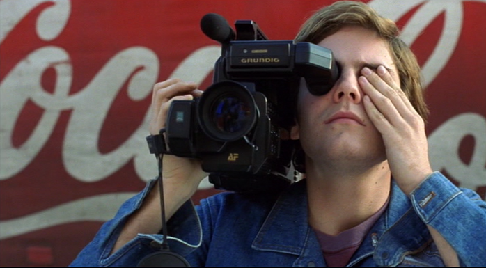 Alex mit Videokamera vor Coca-Cola-Werbung in Nahaufnahme