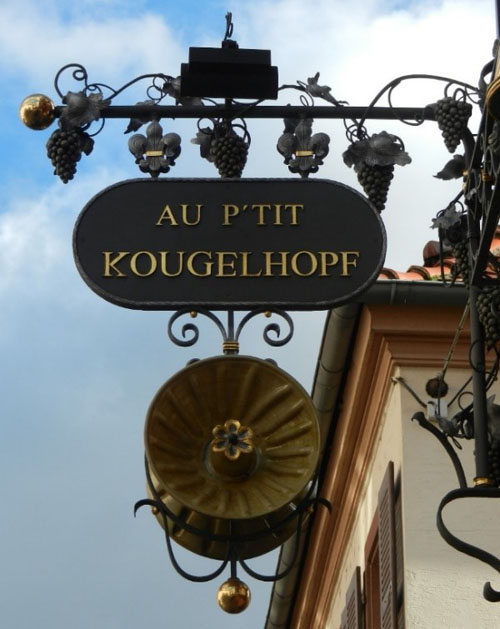 Das Bild zeigt ein kunstvolles Gasthausschild mit der Aufschrift Au P'tit Kougelhopf