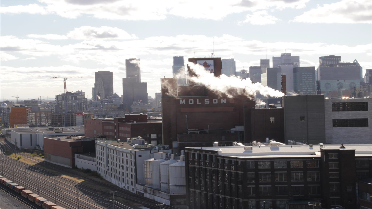 Blick auf die Molson-Brauerei in Montreal mit rauchenden Schornsteinen, vor der Skyline der Stadt.