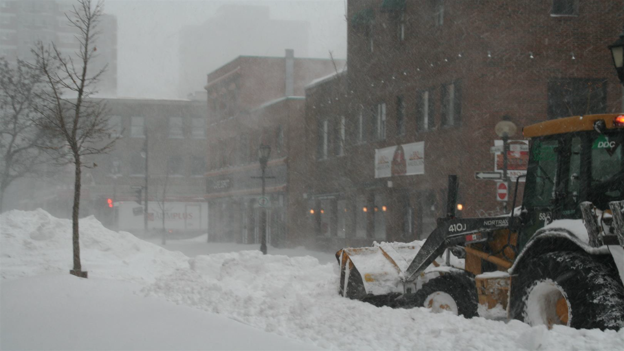 Ein Radlader räumt eine verschneite Straße in einer Stadt während eines Schneesturms