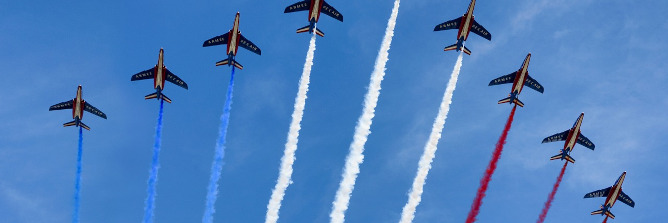 mehrere Kunstflugzeuge fliegen versetzt nebeneinander und hinterlassen Kondenzstreifen in den Farben der französischen Flagge