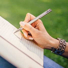 Frau sitzt auf einer Wiese und schreibt etwas in ein Büchlein