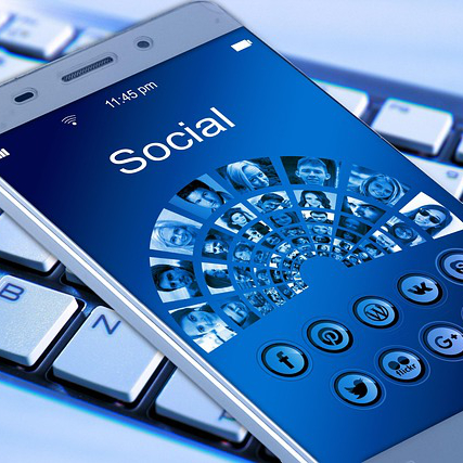 Ein Smartphone liegt auf einer Tastatur. Das Display zeigt das Wort „Social“ und symbolisiert verschiedene Social-Media-Plattformen.